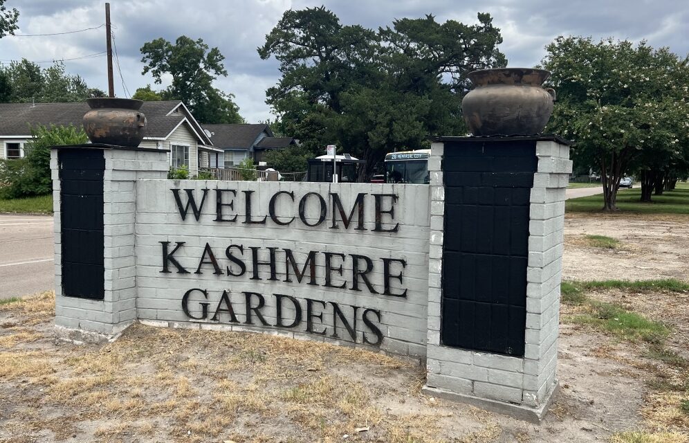 White brick weclome sign flanked by brick columns topped with brown urns. The sign reads "Welcome to Kashmere Gardens"